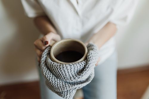 Free Close-up of hands holding a cup wrapped in a knitted scarf indoors. Stock Photo