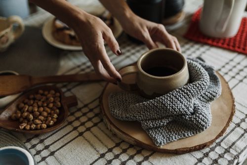 Free Hands arranging a coffee mug on a knitted cloth with nuts on a wooden board. Stock Photo