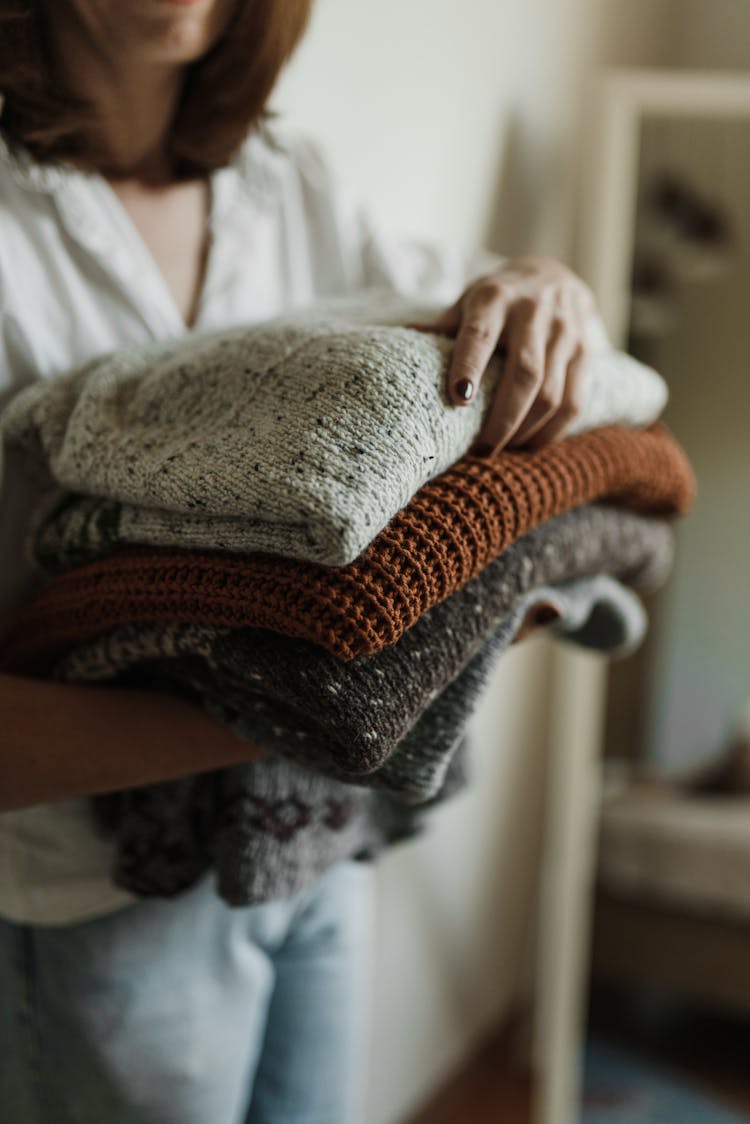 Woman Holding A Bunch Of Knitted Sweaters