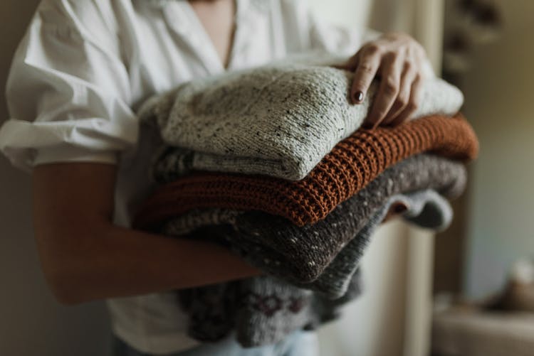 A Person In White Shirt Holding A Stack Of Folded Knitted Fabrics