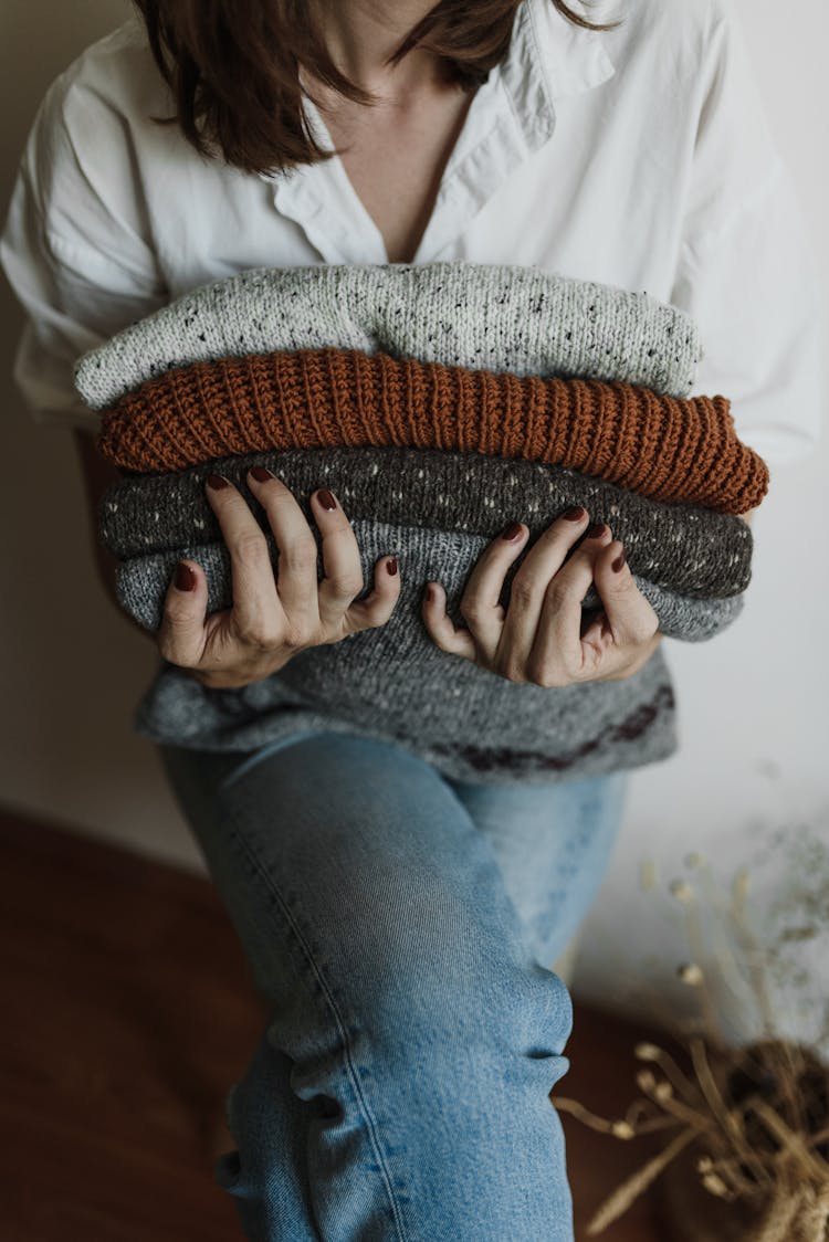 A Person Sitting Holding A Stack Of Folded Knitted Fabrics
