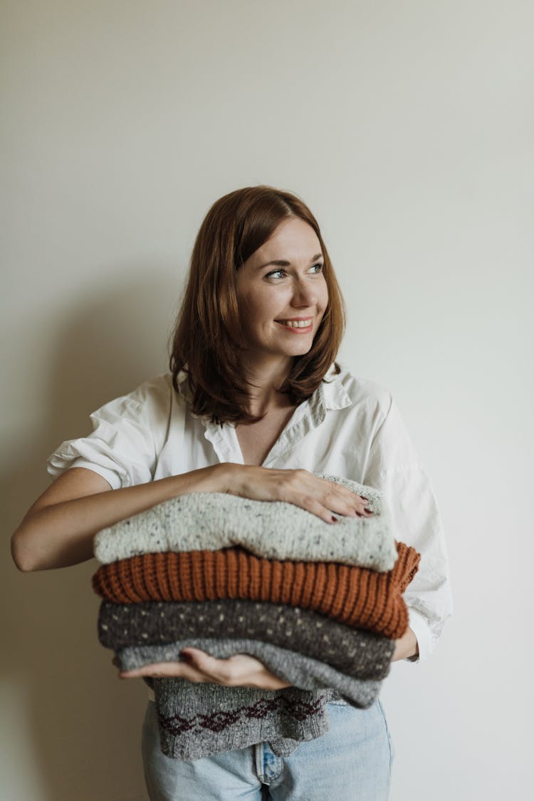 A Woman Sitting Holding A Stack Of Folded Knitted Fabrics
