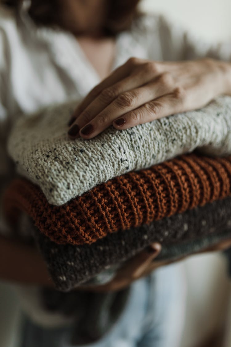 A Close-up Shot Of A Person Holding A Stack Of Folded Knitted Fabrics
