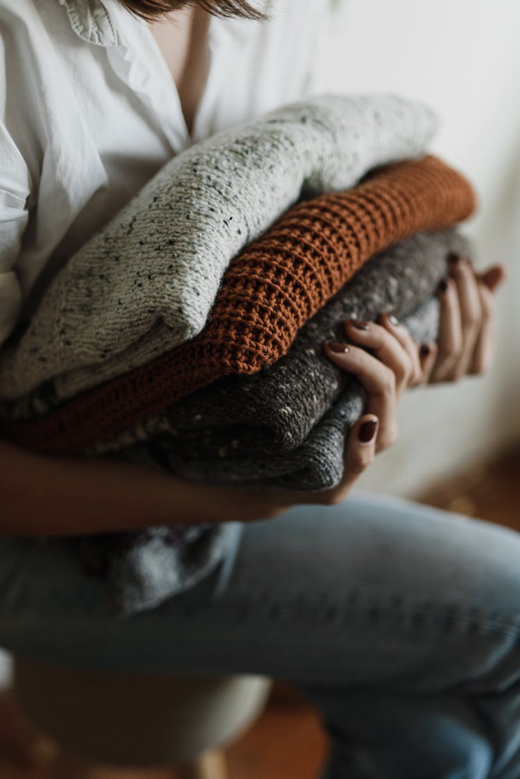 A Close-up Shot Of A Person Holding A Stack Of Folded Knitted Fabrics
