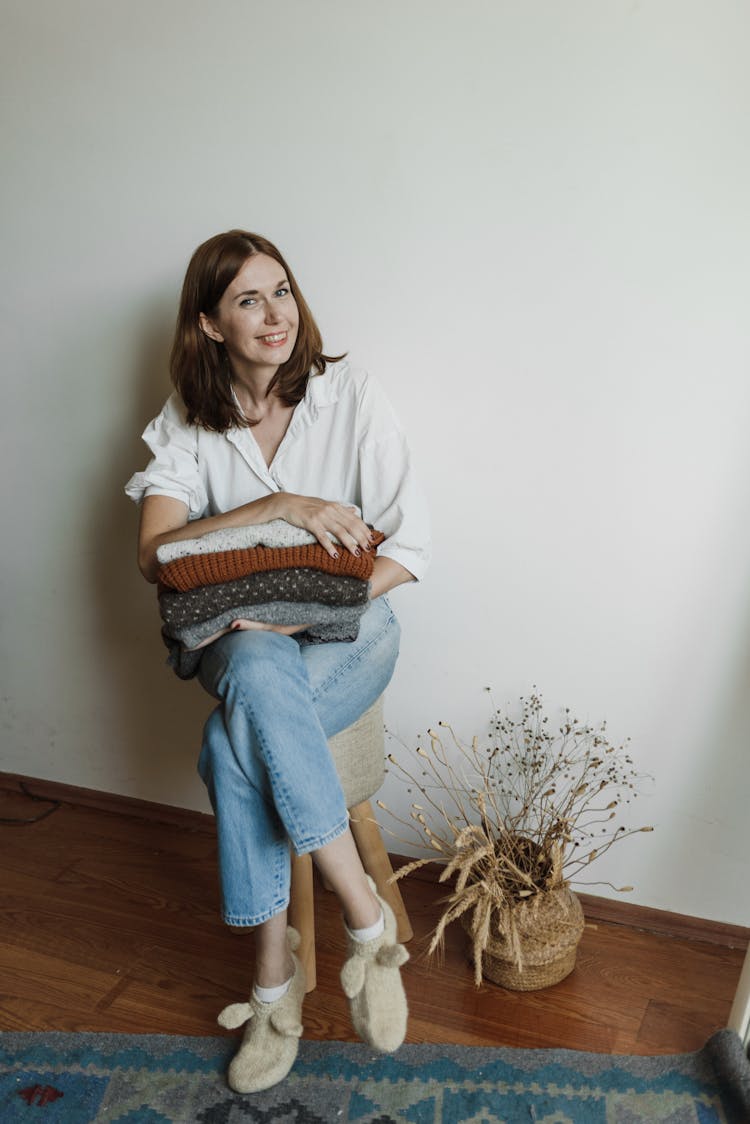 A Woman Sitting Holding A Stack Of Folded Knitted Fabrics
