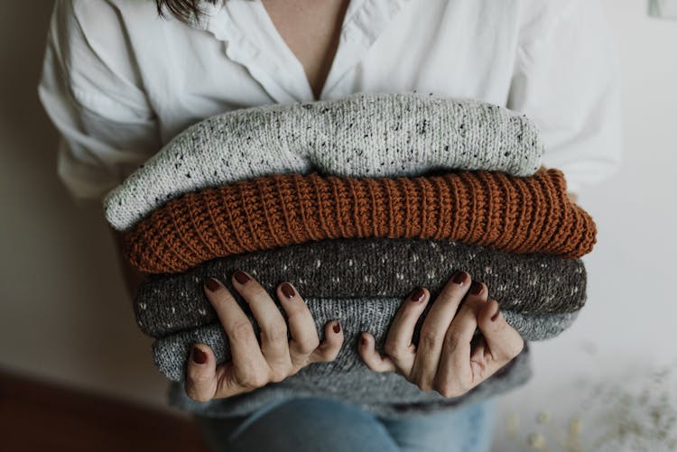 A Close-up Shot Of A Person Holding A Stack Of Folded Knitted Fabrics
