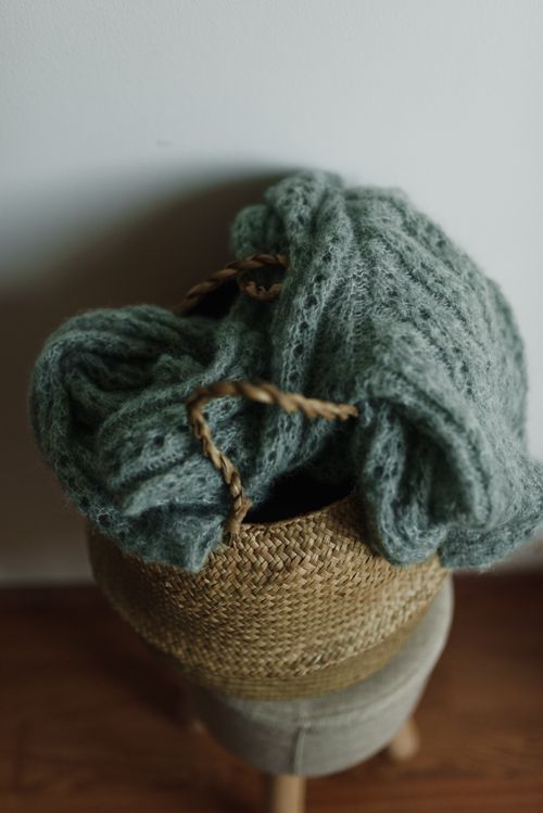 Free A close-up view of a green knitted sweater in a woven basket, ideal for home decor stock photos. Stock Photo