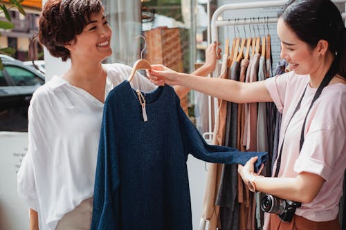 Crop Asian buyer with girlfriend selecting clothes in street shop