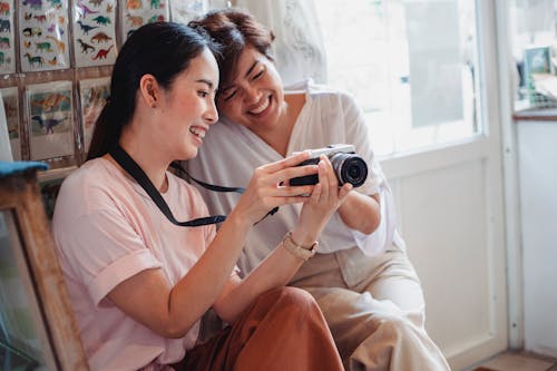 Happy Asian girlfriends sharing photo camera in shop