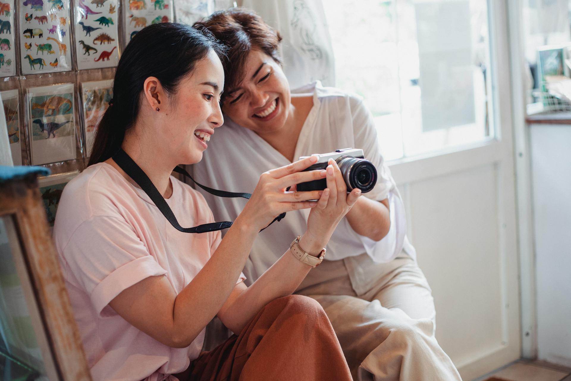 Two cheerful women looking at photos on a camera, sharing joyful moments indoors.