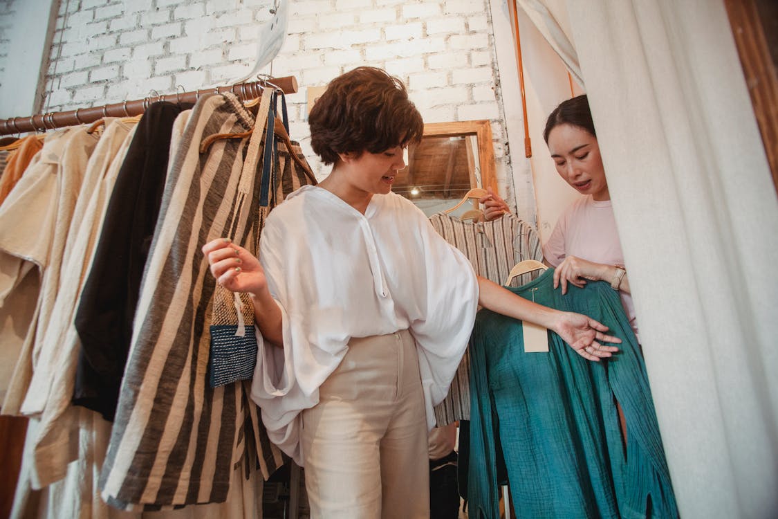 Low angle of stylish young ethnic female friends in trendy outfits choosing clothes in fashion boutique