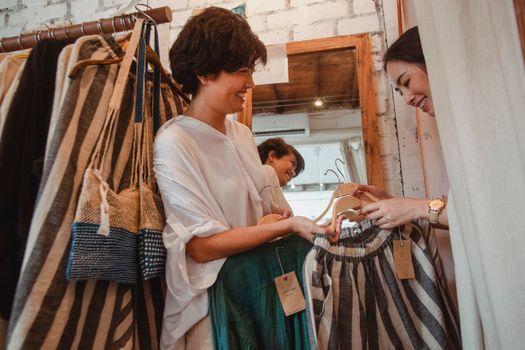 在时尚商店里，一位开朗的年轻亚洲女顾客正微笑着挑选衣服，这是她的侧视图