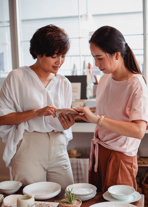 Free Concentrated young ethnic female friends in trendy clothes choosing elegant ceramic dishware in modern store Stock Photo