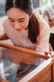 High angle of crop young Asian female costumer with long dark hair choosing wristwatches while standing near glass display shelf in modern store