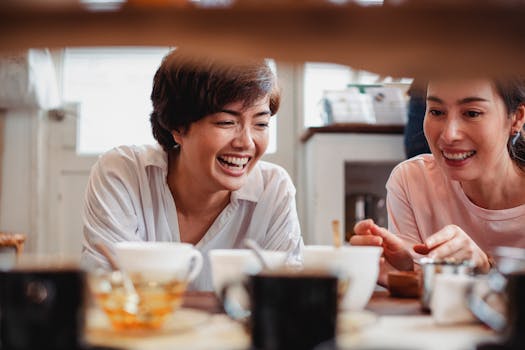 Two women sharing laughter and joy over coffee cups in a cozy cafe setting.