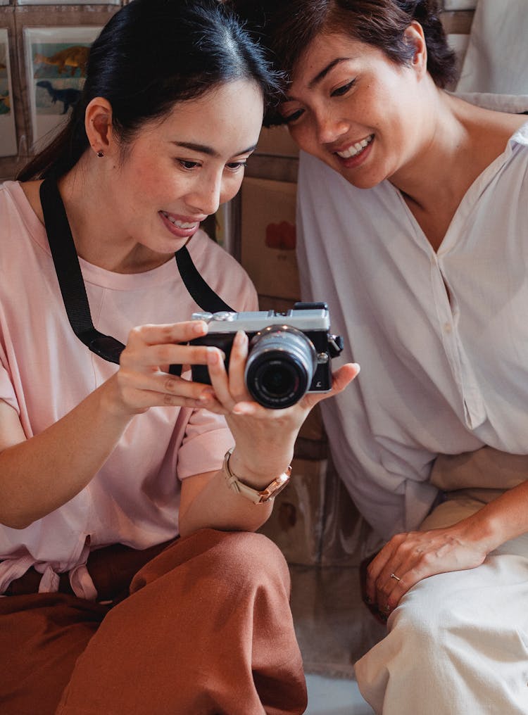 Positive Young Ethnic Females Watching Pictures On Photo Camera