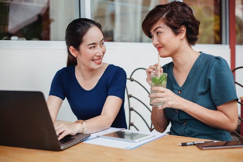 Happy Asian woman drinking cocktail while working with colleague