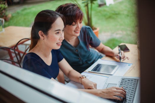 Two young women collaborating on a business project outdoors with laptops and documents.