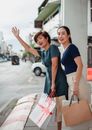 两个快乐的女人在城市街道上挥舞着购物袋叫出租车