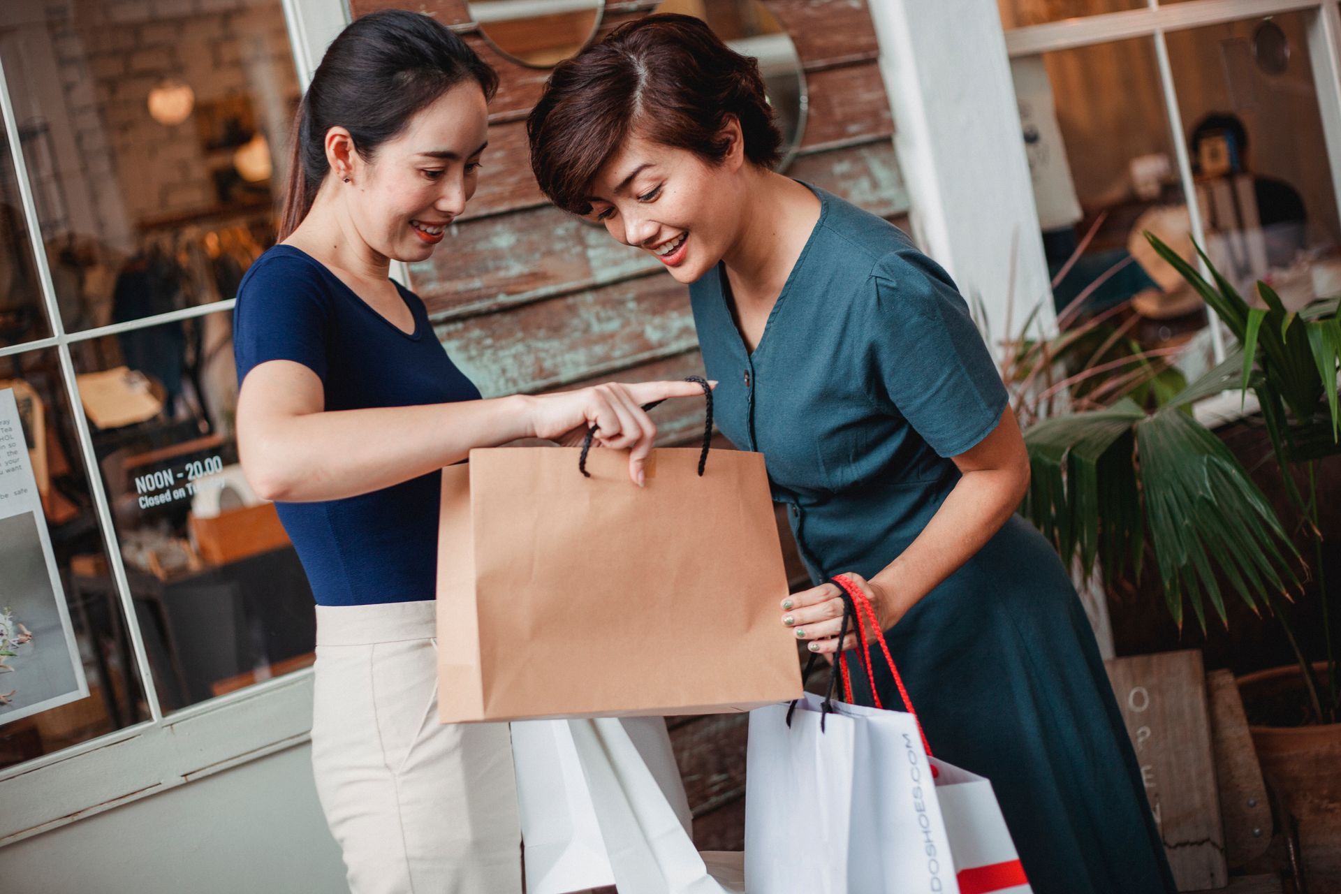 Happy ethnic female friends with shopping bags smiling while demonstrating goods to each other