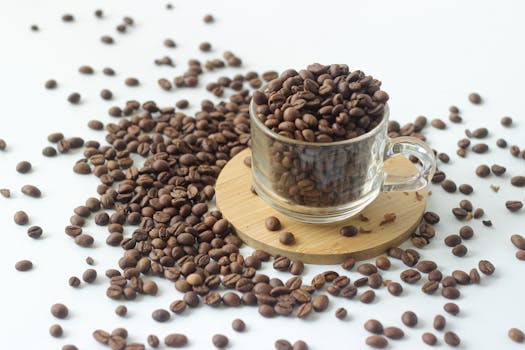 Glass cup filled with coffee beans spilling onto a white surface. Perfect for coffee lovers.