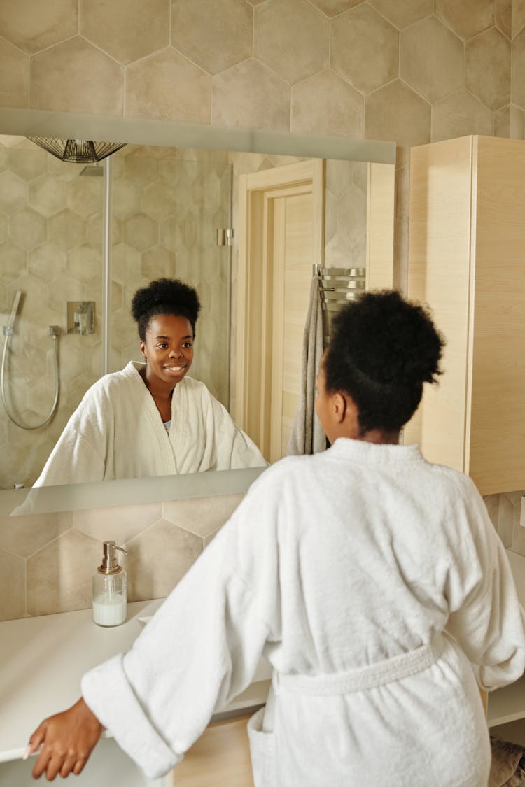 A Woman In A Bathrobe Looking At The Mirror