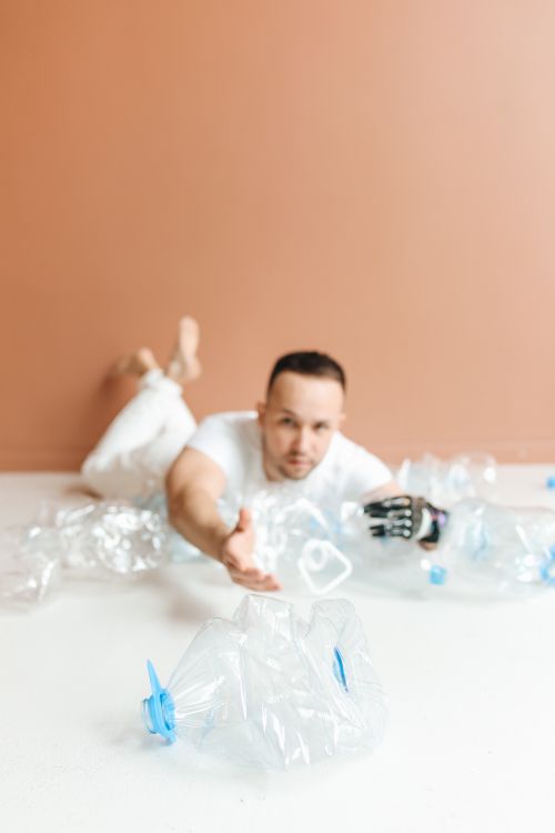 Free Caucasian man with prosthetic hand reaching for empty plastic bottles in studio setting. Stock Photo