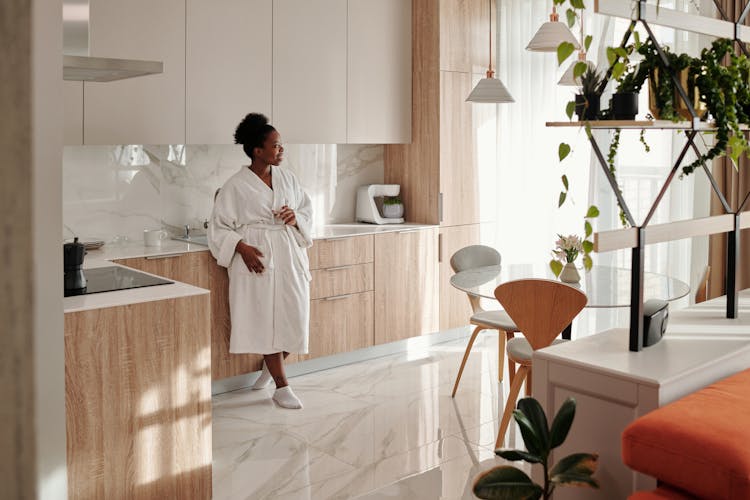 Woman In White Bathrobe Leaning On Kitchen Counter