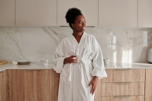 Adult woman in a bathrobe holding a glass, enjoying a relaxed morning in a modern kitchen.