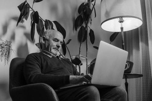 Grayscale Photo of an Elderly Man Using a Laptop 