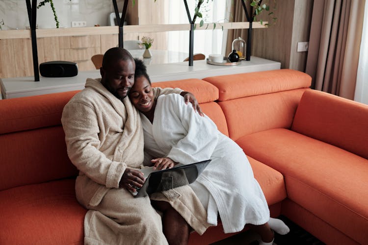 Couple Sitting On Orange Couch Using Laptop