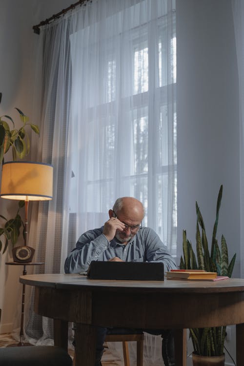 Focused Elderly Man sitting beside a Wooden Table 