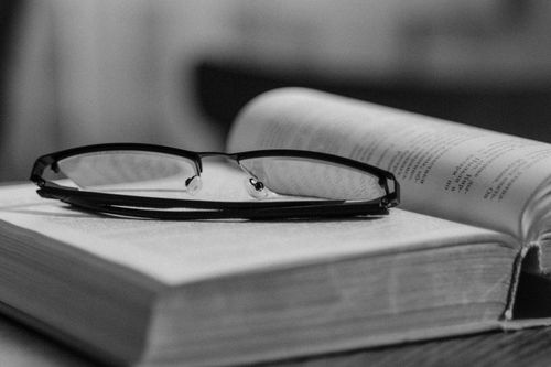 Free Black and white photo of eyeglasses resting on an open book, creating a minimalist and classic feel. Stock Photo