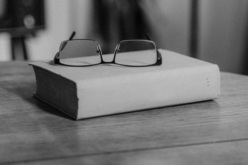 Free Black and white image of eyeglasses resting on a closed book on a wooden table. Stock Photo