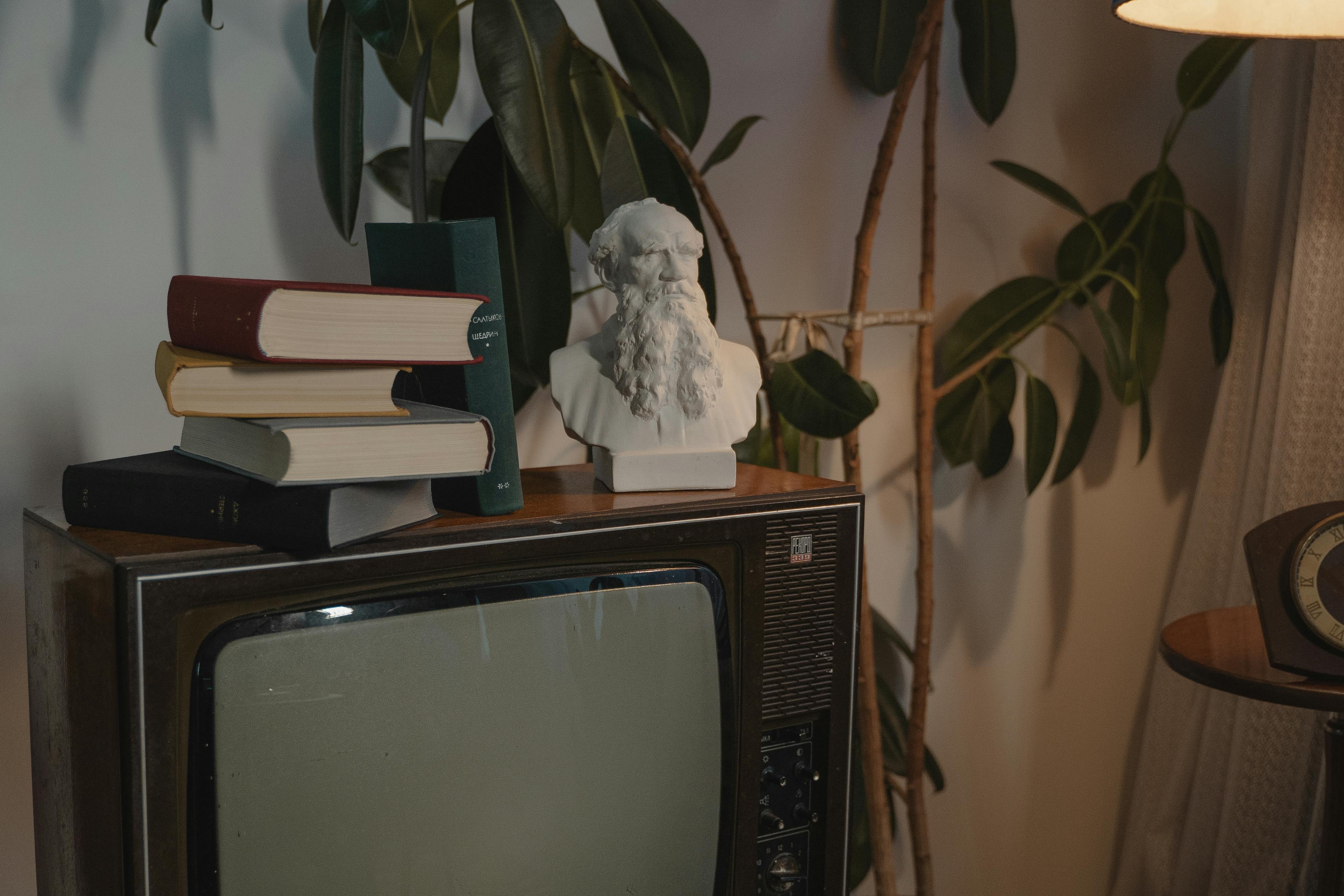 stacked books and a head bust on top of crt television