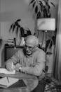 Monochrome Photo of an Elderly Man Writing on a Journal