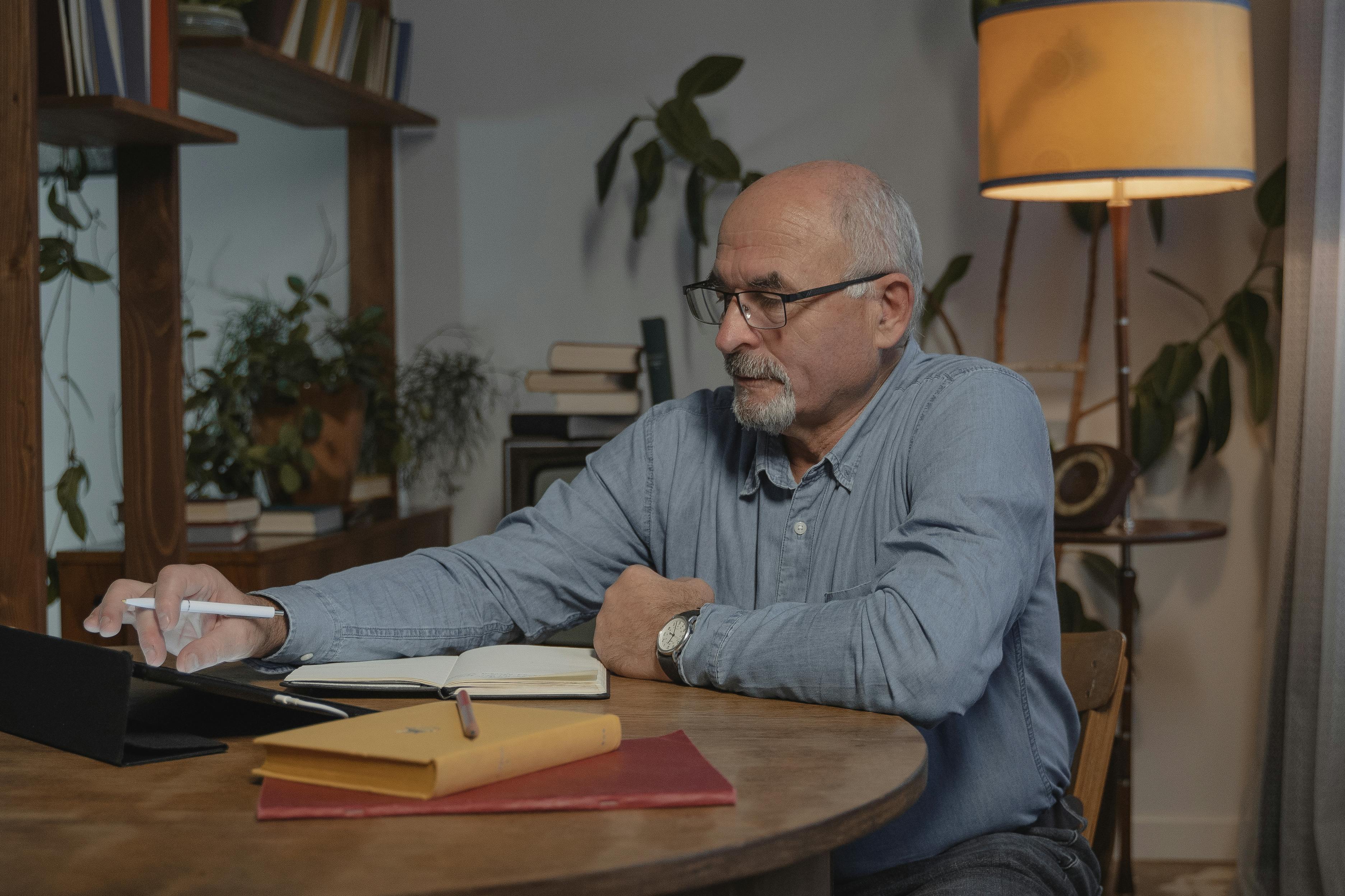 man in blue dress shirt wearing black framed eyeglasses sitting at brown wooden table