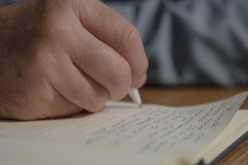 Close-Up of a Person Writing on a Notebook 