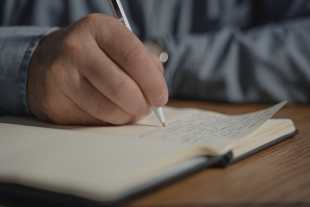 Person writing in journal for self-reflection and recovery planning