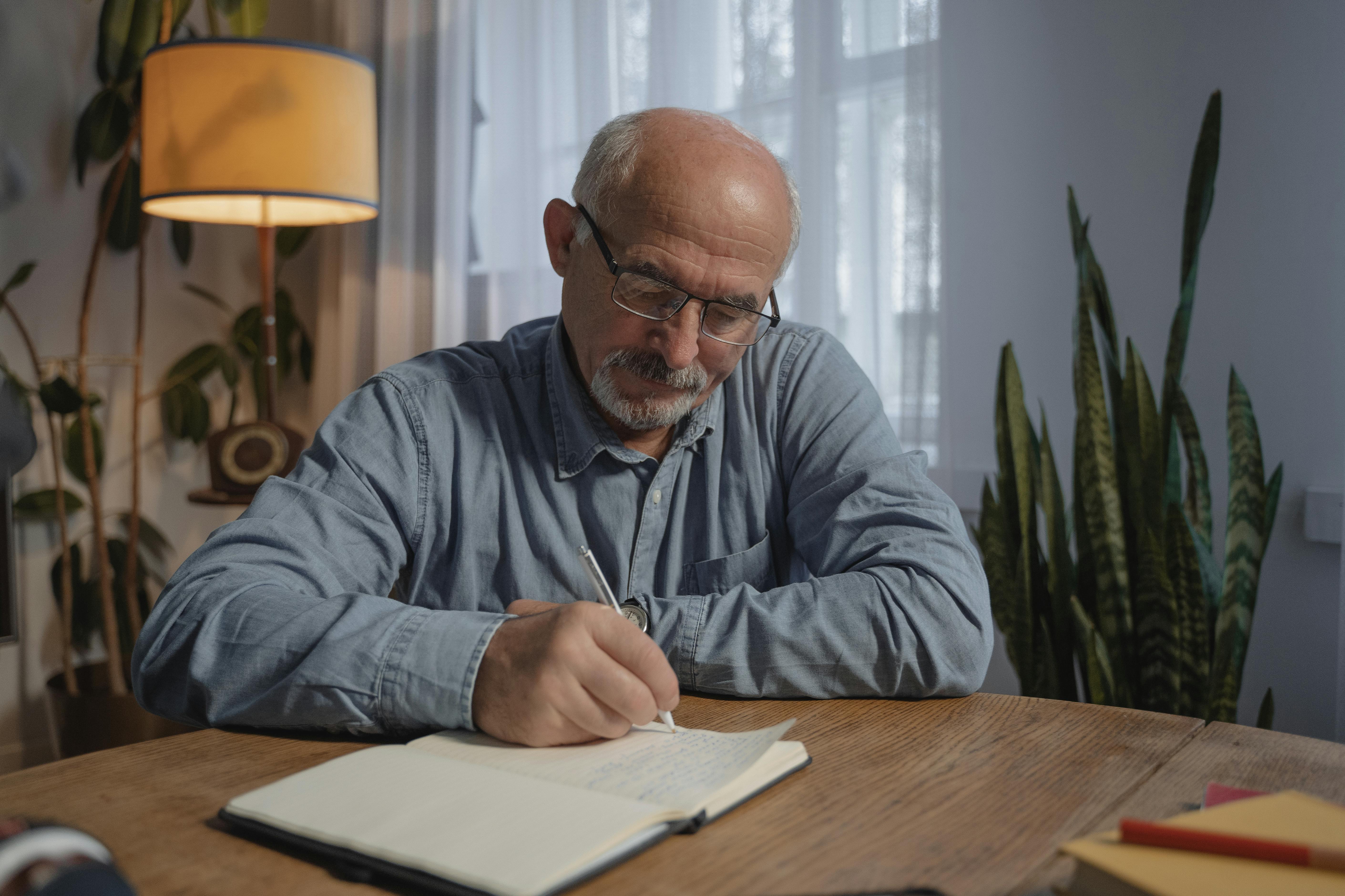 man in gray dress shirt wearing black framed eyeglasses writing on white paper