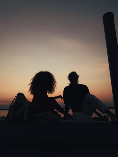 Free Silhouettes of anonymous friends sitting on street and enjoying picturesque sunset while spending time together Stock Photo