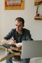 A Man in Plaid Long Sleeves Holding a Pen while Looking at the Pages of the Notebook he is Holding