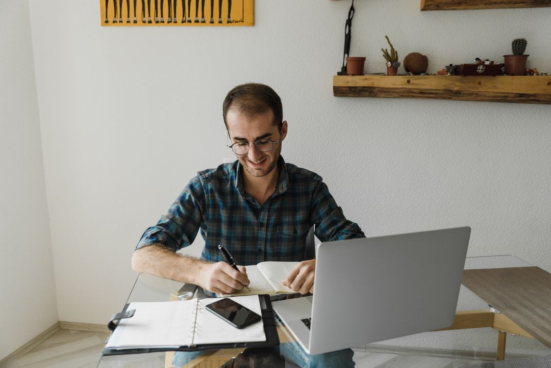 Smiling Man Writing in Notebook, in Home Office · Free Stock Photo