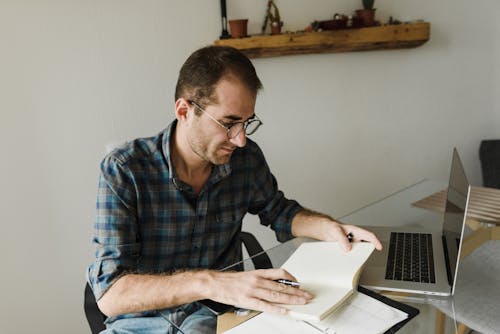 A Man Holding a Notebook Near a Laptop