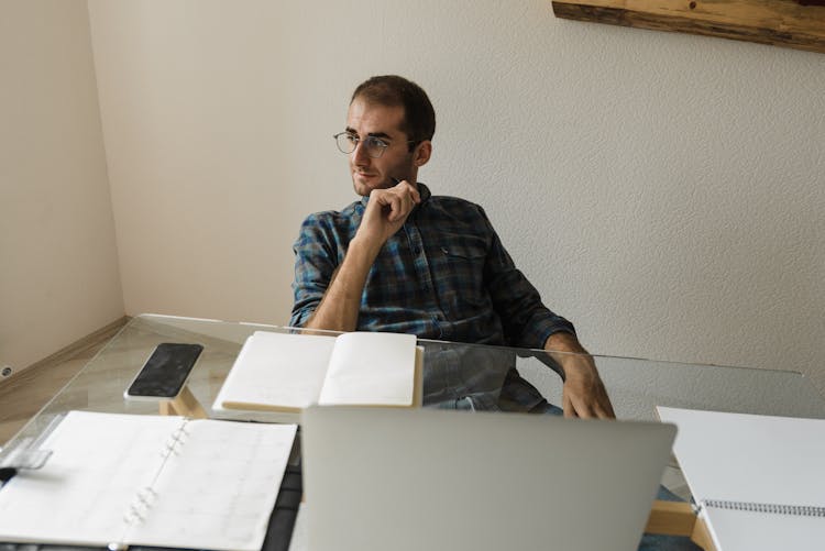 A Man With Eyeglasses Sitting Near A Notebook