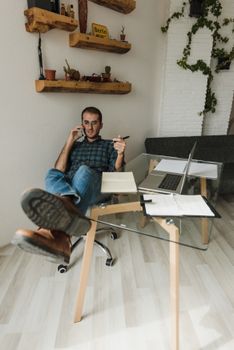 A man talking on the phone while working from home at a glass table. Indoor setting.