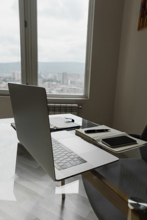 Free Silver Laptop on Top of Glass Table Near the Windows Stock Photo