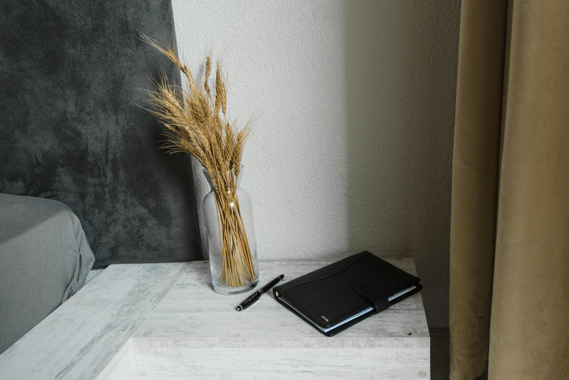 A cozy and modern bedroom corner with dried plants, a vase, and a planner on a bedside table.