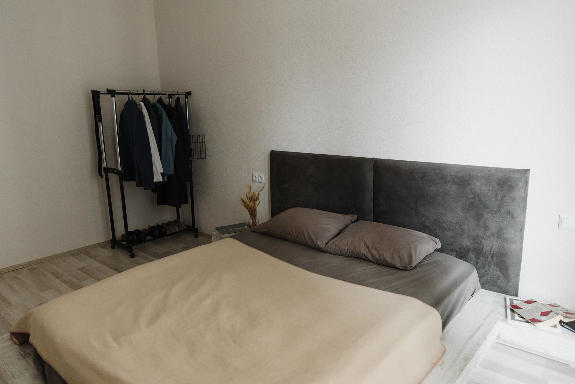 minimalist apartment organization for cozy homes A minimalist bedroom featuring a stylish gray headboard, beige bedding, and a simple clothes rack for a modern look.