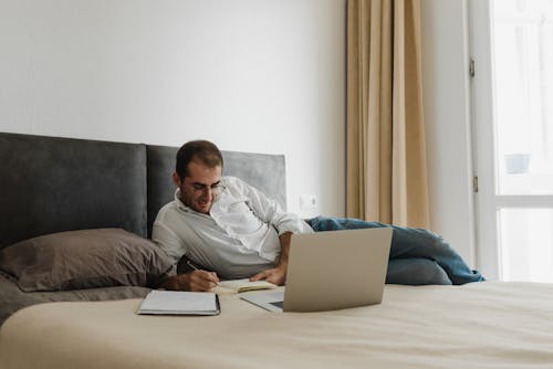 無料 Macbookを使用して灰色のソファに座っている白いドレスシャツの男 写真素材